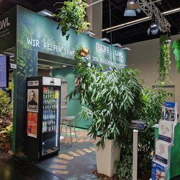 Der LWL Stand auf der Zukunft Personal 2025. Dunkelgrüner Messestand mit Dschungel Pflanzen im Vordergrund.