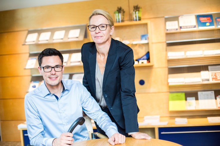 Eine Frau und ein Mann stehen nebeneinander. Der Mann hält ein Telefon in der Hand.