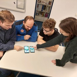 Menschen sitzen vor einem Handy mit der App "Glücklich-App"