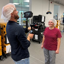 Ein Bild des Drehtages zur Videostory. Es ist ein Mann mit einer großen Filmkamera zu sehen, vor ihm steht eine Frau.